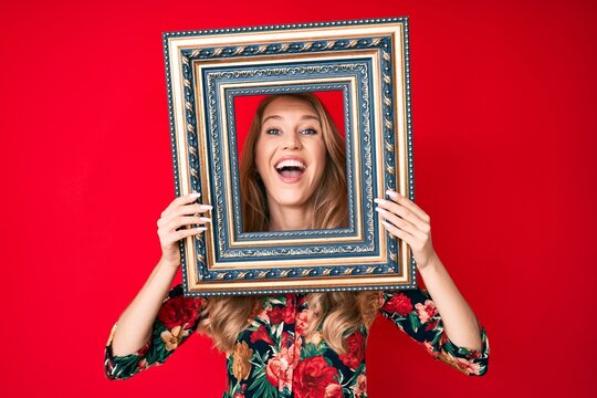Young caucasian woman with blond hair holding empty frame smiling and laughing hard out loud because funny crazy joke.