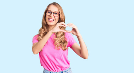 Young beautiful caucasian woman with blond hair wearing casual clothes and glasses smiling in love doing heart symbol shape with hands. romantic concept.