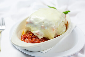 A view of a casserole dish of a large slice of lasagna with melted mozzarella cheese on top, in a restaurant or kitchen setting.