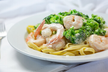 A view of a plate of broccoli shrimp Alfredo, in a restaurant or kitchen setting.