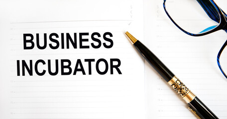 In the notebook is the text of BUSINESS INCUBATOR, next to the pen and glasses.