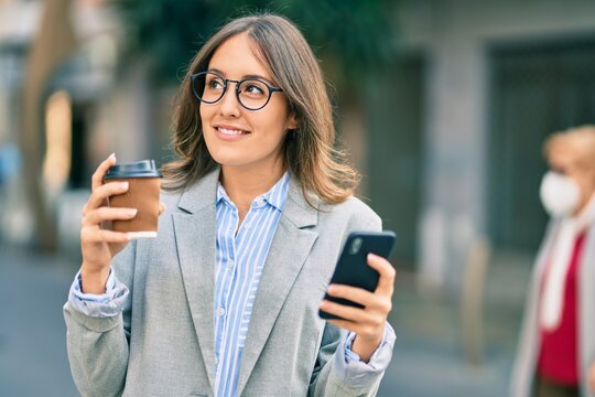 Young hispanic businesswoman using smartphone and drinking take away coffee at the city.
