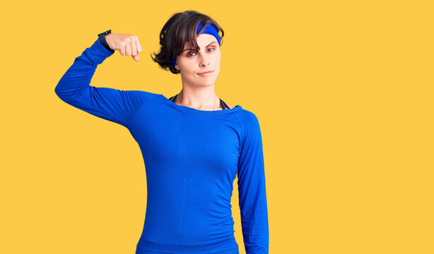 Beautiful young woman with short hair wearing training workout clothes strong person showing arm muscle, confident and proud of power