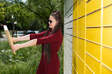 A young teenager in dark glasses has picked up the package from a parcel locker and is trying to read the sender and find out who made her surprise.