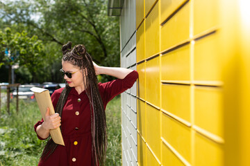 A young teenager in dark glasses has picked up the package from a parcel locker and is trying to...