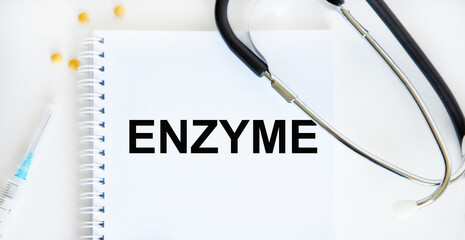 In the notebook is the text OF ENZYME, next to the stethoscope, yellow tablets and syringe.