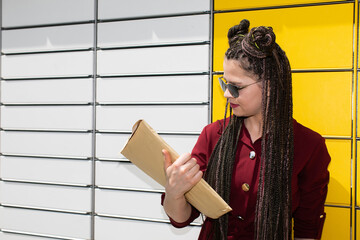 A young teenager in dark glasses has picked up the package from a parcel locker and is trying to...