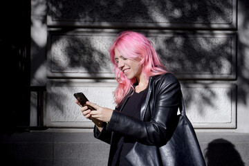 mujer vestida con abrigo de piel negro sonriendo mientras escribe un mensaje en su mobil