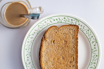 Café da manhã; Uma torrada dentro de um prato e uma xícara de leite com café.
