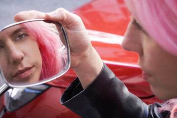 chica de pelo rosa mirandose en el retrovisor de una moto en la calle