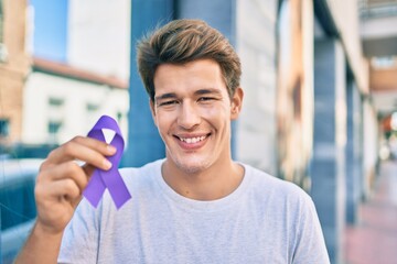 Young caucasian man smiling happy holding purple ribbon at the city.