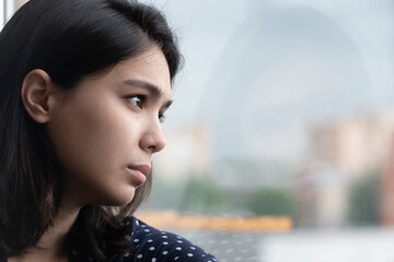 Close up frustrated thoughtful Asian woman looking out window, thinking about personal problems,...