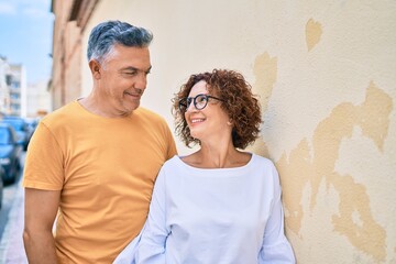 Middle age couple smiling happy leaning on the wall at street of city.