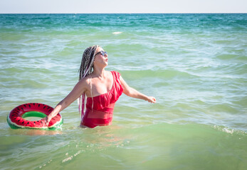 A cheerful middle-aged woman with a watermelon wedge swimming circle swimming in a sea. The concept of leisure and entertainment