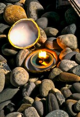 Small oval open box made of natural shell sashes with a burning candle inside on sea pebbles at dusk