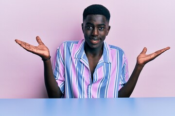 Young african american man wearing casual clothes sitting on the table clueless and confused...
