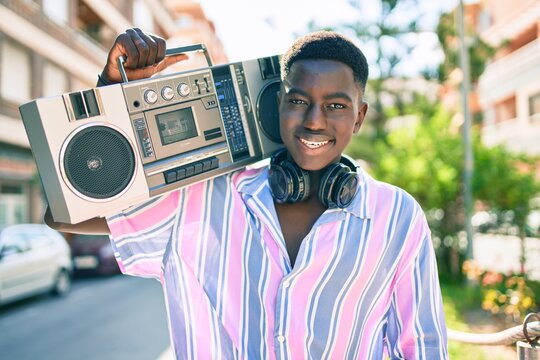 Young african american man listening to music using boom box and headphones walking at street of city.