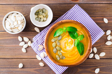 Top view of Vegetarian autumn pumpkin puree soup with seeds, basil and cream in a wooden plate on the table. Rustic style