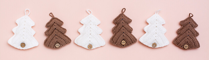 Christmas handmade. Knitted fir-trees in a row on a pastel background. Handicraft and leisure. Web banner
