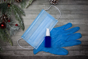 Mask, gloves and antiseptic lie on a wooden background and a branch of a Christmas tree. New Year's mood is in quarantine