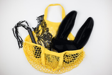 BDSM sex toys for adults. Yellow bag from sex shop with whip, mask and bandage on white background