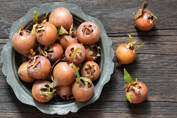 Fresh ripe organic common medlar fruit in plate or bowl on wooden rustic background. Healthy food Mespilus germanica
