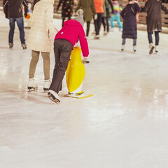 Ice rink. Mom teaches doughter to skate, girl holds a penguin for support. Winter family activities, sport concept