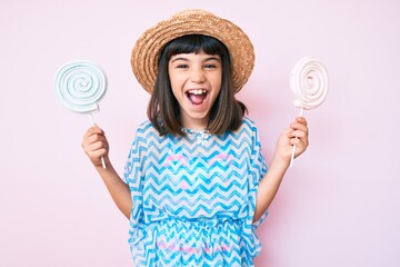 Young little girl with bang wearing summer dress eating candy smiling and laughing hard out loud...