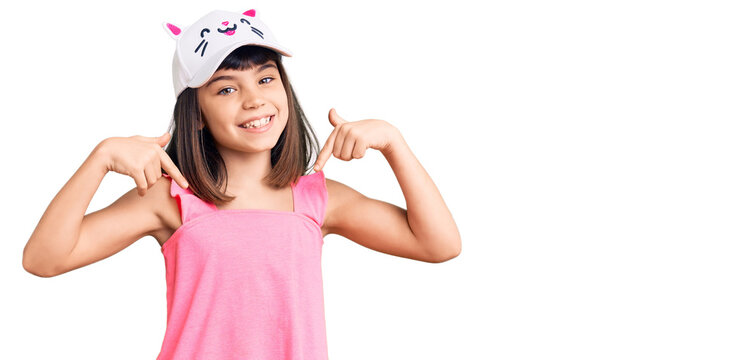 Young little girl with bang wearing funny kitty cap looking confident with smile on face, pointing oneself with fingers proud and happy.
