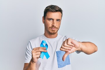 Handsome caucasian man holding blue ribbon with angry face, negative sign showing dislike with...