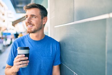 Young caucasian man using smartphone and drinking take away coffee at the city.