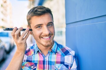 Young caucasian man smiling happy listening audio message using smartphone at the city.