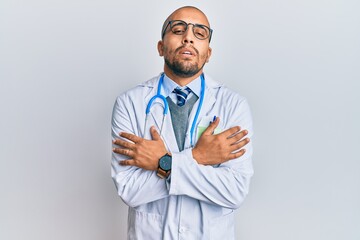 Hispanic adult man wearing doctor uniform and stethoscope shaking and freezing for winter cold with sad and shock expression on face