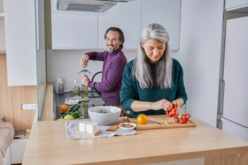 Handsome man and attractive senior woman are making salad