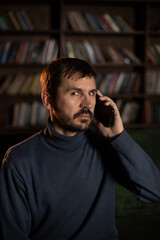 Young bearded man sitting on sofa with phone in hand in dark interior