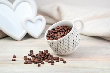 Coffee beans spill out of a tilted Cup on a light background. Side view. Concept of coffee backgrounds.
