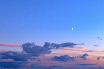 Evening sunset sky with painted clouds in the setting sun and with a crescent moon