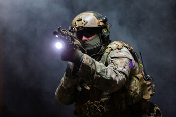 Portrait of army soldier in military camouflage uniform, helmet, glasses and mask holds rifle near...