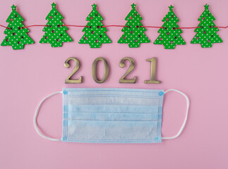 Christmas 2021. Coronavirus new year minimal concept. Flat lay with face masks, metal numbers and pattern christmas trees on pink background. Top view, copy space