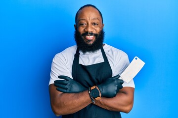 Young african american man wearing professional apron holding knife smiling with a happy and cool...