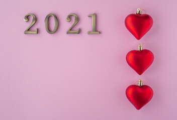 Christmas 2021. Coronavirus new year minimal concept. Flat lay with metal numbers and red hearts balls on pink background. Top view, copy space