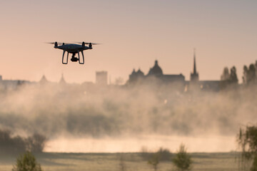 Fototapeta premium Quadcopter in flight on the background of the architecture of the old city of Lutsk (Ukraine) and the fog over the river Styr. Morning.