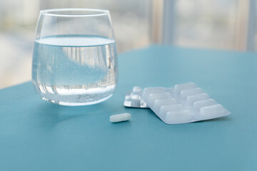 round glass with pure water and white pills in blister on blue table near window, recovery measures. Treatment from headaches, flu, influenza, viruses. Healthcare concept