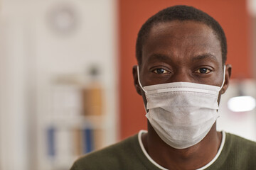 Close up portrait of adult African-American man wearing mask and looking at camera while working in office, copy space
