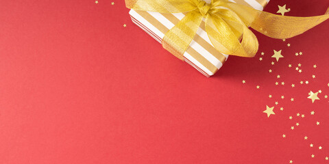 Christmas holiday composition. Gold gift box with ribbon, confetti, Xmas decorations on red...