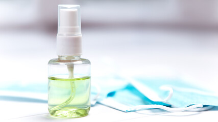 Close up image of small bottle antiseptic hand sanitizer hygiene spread protection with blue face travel surgical disposable mask on the desk, coronavirus prevention disease flu cold weather.
