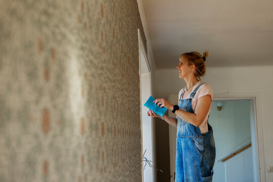 Woman sticking wallpaper on wall, Sweden