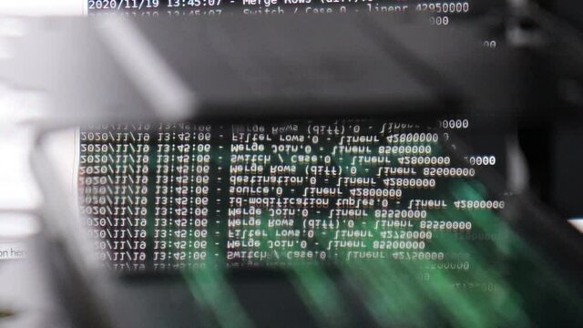 White computer software code moving on a black monitor reflect on glass. Abstract computer hacking in process with rack server base, dynamic text running and flowing on pc screen