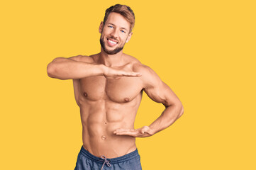 Young caucasian man standing shirtless gesturing with hands showing big and large size sign, measure symbol. smiling looking at the camera. measuring concept.