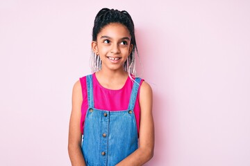 Young african american girl child with braids wearing casual clothes over pink background looking away to side with smile on face, natural expression. laughing confident.